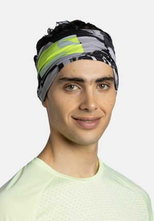 Joven con cabello corto y oscuro, lleva una cinta para la cabeza con patrón gris, negro y verde neón y una camiseta deportiva de color amarillo claro, sonriendo ligeramente.