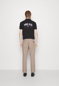 Sort polo-shirt med "TOMMY JEANS" og "NEW YORK CITY" trykt på bagsiden, kombineret med beige bukser og sorte sko.