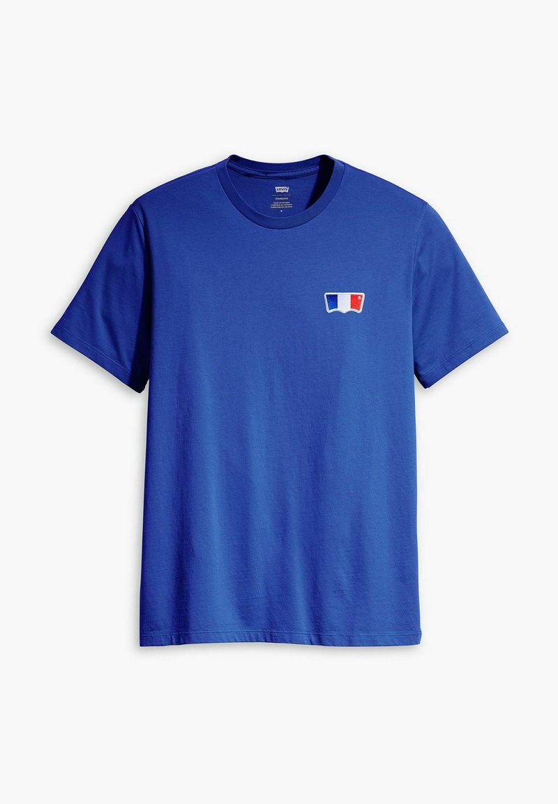 Camiseta de algodón azul con mangas cortas y cuello redondo. Presenta un pequeño logo en blanco, azul y rojo en la parte izquierda del pecho.