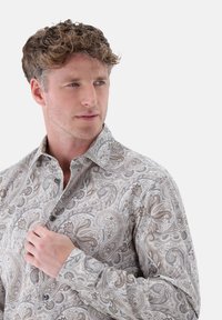 Long-sleeve button-up shirt in light beige with intricate paisley pattern in blue and brown tones, featuring a spread collar and textured fabric.