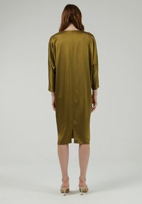 Vestido de satén verde oliva con un corte relajado, mangas tres cuartos y una abertura en la espalda, que presenta un cierre tipo ojal en el cuello.