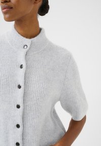 Hele hall hüübi džemper lühikeste varrukatega, kõrge kraega, ribakujuline tekstuur ja mustad nupud ees. Pehme ja udune materjal.