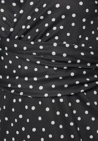 Černá látka s bílými puntíky, s drapovaným designem a jemnou strukturou. Materiál se zdá být hladký a lehký.