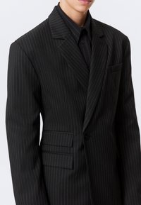 Svart rutete dress med spiss krage, enkel knappelukking og to frontlommer; har en glatt tekstur og en skreddersydd passform.