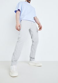 Ljusblå kortärmad t-shirt, grå slim-fit byxor och vita sneakers med pastellfärger, mot en vit bakgrund.