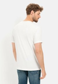 Hvid kortærmet t-shirt lavet af glat bomuld, med en klassisk rund hals og en afslappet pasform, parret med blå denim jeans.