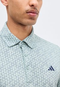 Κοντινό πλάνο ενός ατόμου που φοράει ανοιχτό μπλε πόλο πουκάμισο με σχέδιο, κουμπιά και μικρό σκούρο μπλε λογότυπο στην τσέπη του στήθους.