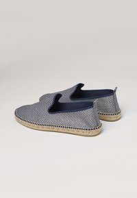 Bottines à carreaux bleus et blancs avec une semelle en jute tissée et des côtés élastiques pour un enfilage facile. Texture lisse avec un minimum de détails.