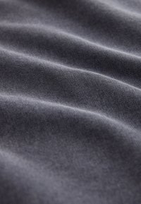 Gros plan sur un tissu gris foncé avec une texture tissée fine et des plis doux créant des ombres délicates.