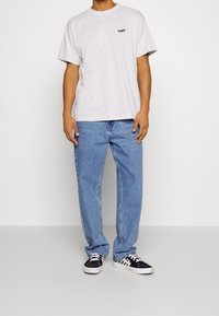 T-shirt en coton gris à manches courtes et col rond, associé à un jean bleu clair. Des baskets à damiers noir et blanc complètent le look.