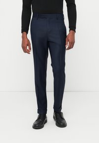 Marineblaue, maßgeschneiderte Hose mit schmaler Passform, flacher Vorderseite und umgeschlagenen Säumen. Glatte Textur, Gürtelschlaufen und diagonale Taschen.