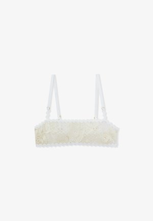 Bralette in pizzo di colore beige chiaro con bordi ondulati, spalline bianche regolabili e dettagli in metallo dorato. Il pizzo presenta motivi floreali.