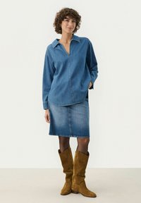 Top in denim con colletto, scollatura a V, maniche lunghe; abbinato a una gonna in denim. Stivali alti fino al ginocchio in suede marrone completano l'outfit.