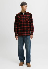 Röd och svart rutad flanellskjorta med långa ärmar och två bröstfickor, tillsammans med blå jeans och bruna slip-in skor.