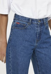 Jeans de denim con un diseño de cintura alta y pierna recta, de color azul y costuras en contraste. Incluye bolsillos delanteros y traseros.