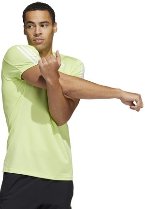Camiseta atlética verde claro de manga corta con una sutil textura acanalada. Presenta rayas blancas en los hombros. Modelo estirando el brazo.
