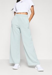 Ljusblå byxor med vida ben, tillverkade av mjukt tyg med resår i midjan och sidfickor; har en liten logodetalj.