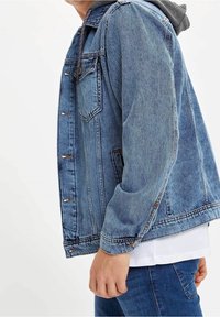 Giubbotto in denim di colore azzurro chiaro con maniche lunghe, chiusura frontale con bottoni e due tasche sul petto. Capitone con fodera interna grigia. Vestibilità casual.