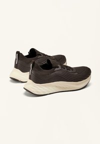 Zwarte sportieve schoenen met een textuur gebreide bovenkant, een lichtgewicht foam tussenzool en een contrasterende crèmekleurige rubberen zool. Minimalistisch ontwerp.