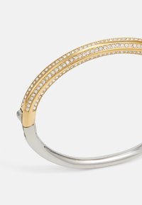Gullfarget armbånd med tre rader av klare rhinstein og en sølvfarget metallbase. Glatt tekstur, buet design, sikker lås.