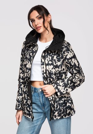 Mujer con una chaqueta con capucha de estampado animal en blanco y negro, top blanco corto y jeans de tiro alto en azul claro.