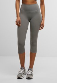 Grå, tettsittende capri leggings med høy midje og glatt stoff; ingen synlige mønstre. Kombinert med grå treningssko.