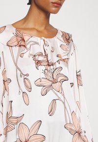 Blusa leggera con motivo floreale in pesca chiaro e crema, caratterizzata da un colletto arricciato e dettagli con cordoncino sullo scollo.
