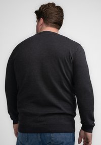 Pulover tricotat de culoare gri închis, cu mâneci lungi, gât rotund și manșete cu model texturat. Textură netedă și design ajustat, purtat cu blugi negri.
