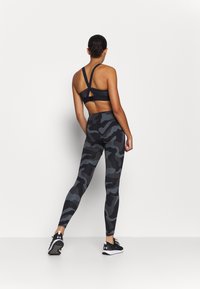 Svarta leggings med camouflage-mönster och matchande sport-bh med korskända remmar, tillverkade av stretchigt material, designade för atletisk användning.