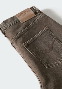 Jeans in denim marrone con una finitura testurizzata, dotati di un'etichetta in pelle e una tasca posteriore con dettagli di cucitura. Piegati e in mostra con una forma slim.