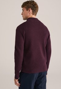 Bordeaux gebreide trui met een textuurafwerking, voorzien van een kraag en lange mouwen. De zoom is geribbeld, wat zorgt voor een passende pasvorm bij de manchetten.