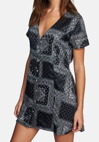 Robe à manches courtes présentant un motif patchwork cachemire noir et blanc, un décolleté en V, et des détails à boutons, confectionnée dans un tissu lisse.