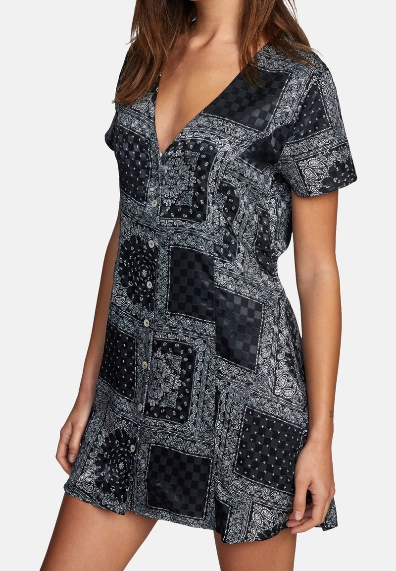 Robe à manches courtes présentant un motif patchwork cachemire noir et blanc, un décolleté en V, et des détails à boutons, confectionnée dans un tissu lisse.