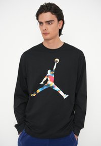 Μαύρη μπλούζα με μακριά μανίκια που διαθέτει πολύχρωμο λογότυπο Jumpman στο μπροστινό μέρος. Φτιαγμένη από μαλακό ύφασμα με χαλαρή εφαρμογή.