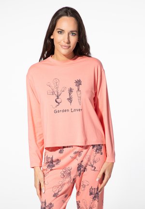 Woman wearing peach-colored long-sleeve shirt and pants with black garden vegetable and plant prints, shirt text reads "Garden Lover."