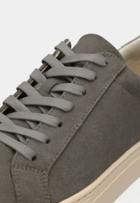 Gros plan d'une basket en suède gris avec des lacets plats assortis et une semelle en caoutchouc beige clair.