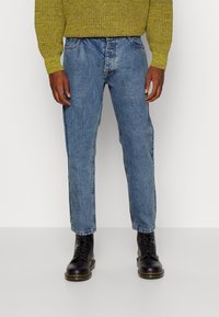 Svetle modré džíny s rovným střihem, pěti kapsami a jemným vyblednutím. V kombinaci s černými šněrovacími botami.