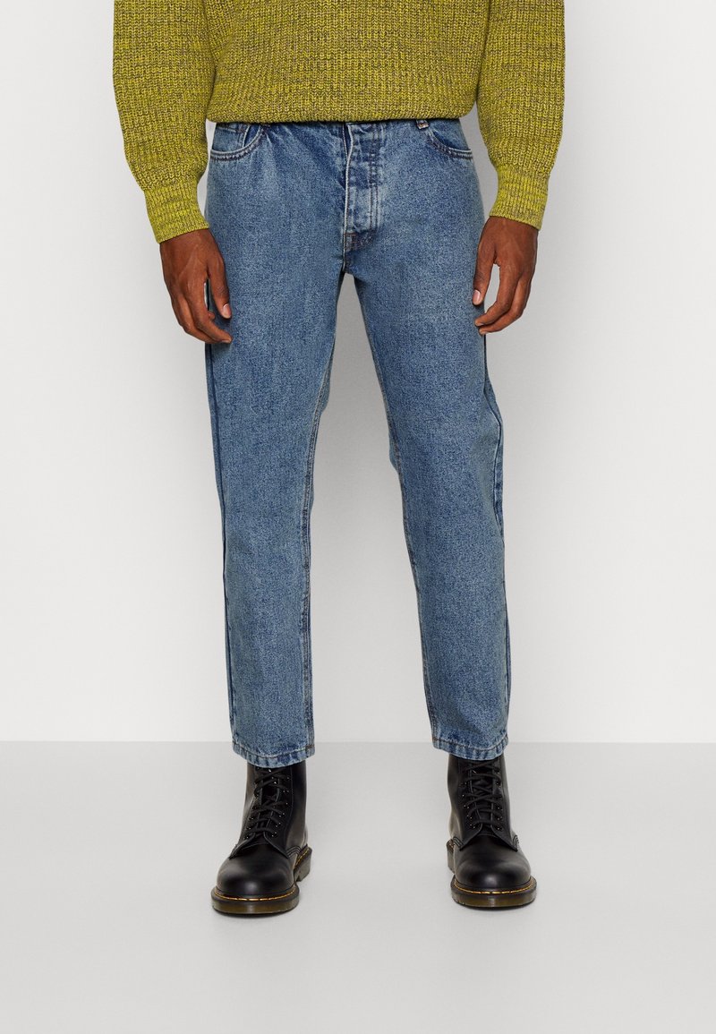 Svetle modré džíny s rovným střihem, pěti kapsami a jemným vyblednutím. V kombinaci s černými šněrovacími botami.