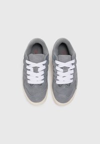 Sneaker in camoscio grigio con lacci bianchi, superficie liscia, punta arrotondata e dettagli testurizzati. Interno morbido e suola a contrasto.