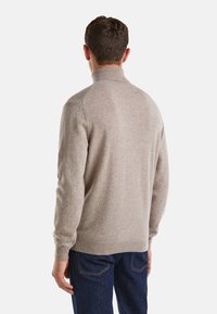 Maglione beige con colletto alto, polsini e orlo a coste. Texture lavorata a maglia con sottili variazioni nello spessore del filato, abbinato a jeans blu scuro.