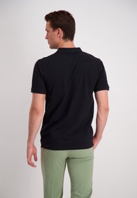 Polo nero con maniche corte, colletto semplice e texture liscia, abbinato a pantaloni su misura verde chiaro.