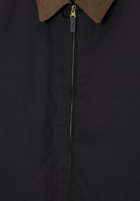 Veste noire avec col en velours côtelé marron et fermeture éclair centrale dorée avec tirette noire.