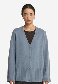 Jasnoniebieski dzianinowy kardigan z dekoltem w serek, ściągaczami na rękawach i dolnym brzegu. Posiada trzy guziki i miękką teksturę.