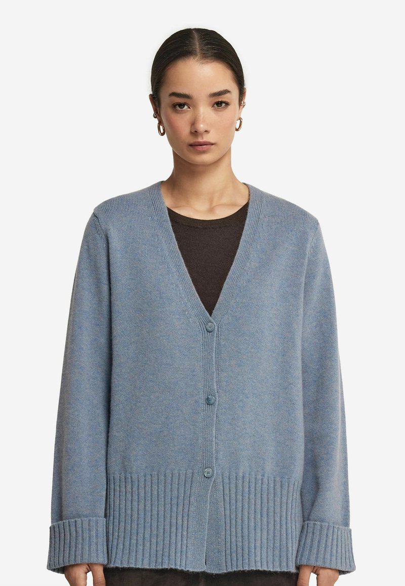 Jasnoniebieski dzianinowy kardigan z dekoltem w serek, ściągaczami na rękawach i dolnym brzegu. Posiada trzy guziki i miękką teksturę.