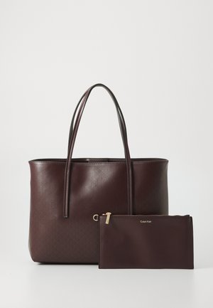 Bolso tote burdeos con textura suave, dos asas largas y un bolsillo extraíble. Ambos presentan un sutil detalle de logo y un patrón geométrico.