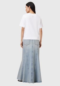 Top bianco a maniche corte con scollo rotondo, abbinato a una lunga gonna in denim azzurro chiaro con forma a campana e dettagli di cucitura visibili.