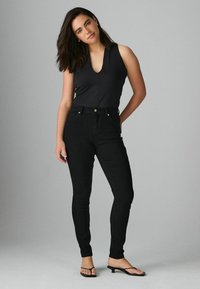 Mustat korkeavyötäröiset farkut, joissa on slim fit, viisi taskua ja napitus. Yhdistetty tiukkaan mustaan hihattomaan paitaan.