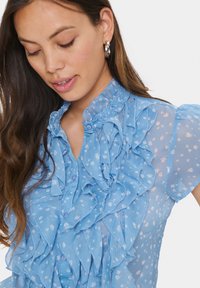 Hellblaue, durchsichtige Bluse mit gerüschtem Vorderteil, floralem Muster, hohem rüschenbesetztem Kragen und kurzen Ärmeln. Sanfte Textur, Knopfverschlüsse.