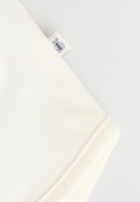 Tissu en coton blanc avec une texture lisse, comportant une petite étiquette avec un logo gris brodé dans le coin. Design simple et minimaliste.