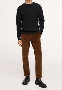 Pull à côtes noir, pantalon en velours côtelé marron et bottines noires. Le pull a un col rond ; le pantalon présente un tissu texturé.